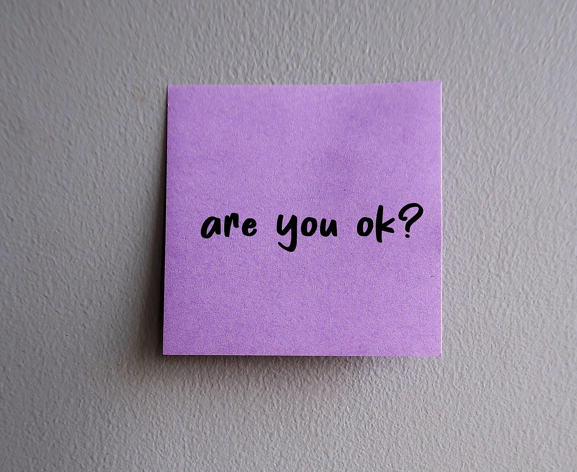 Purple note stick on wall with handwritten text ARE YOU OK?, to ask question to someone you care to show support and help